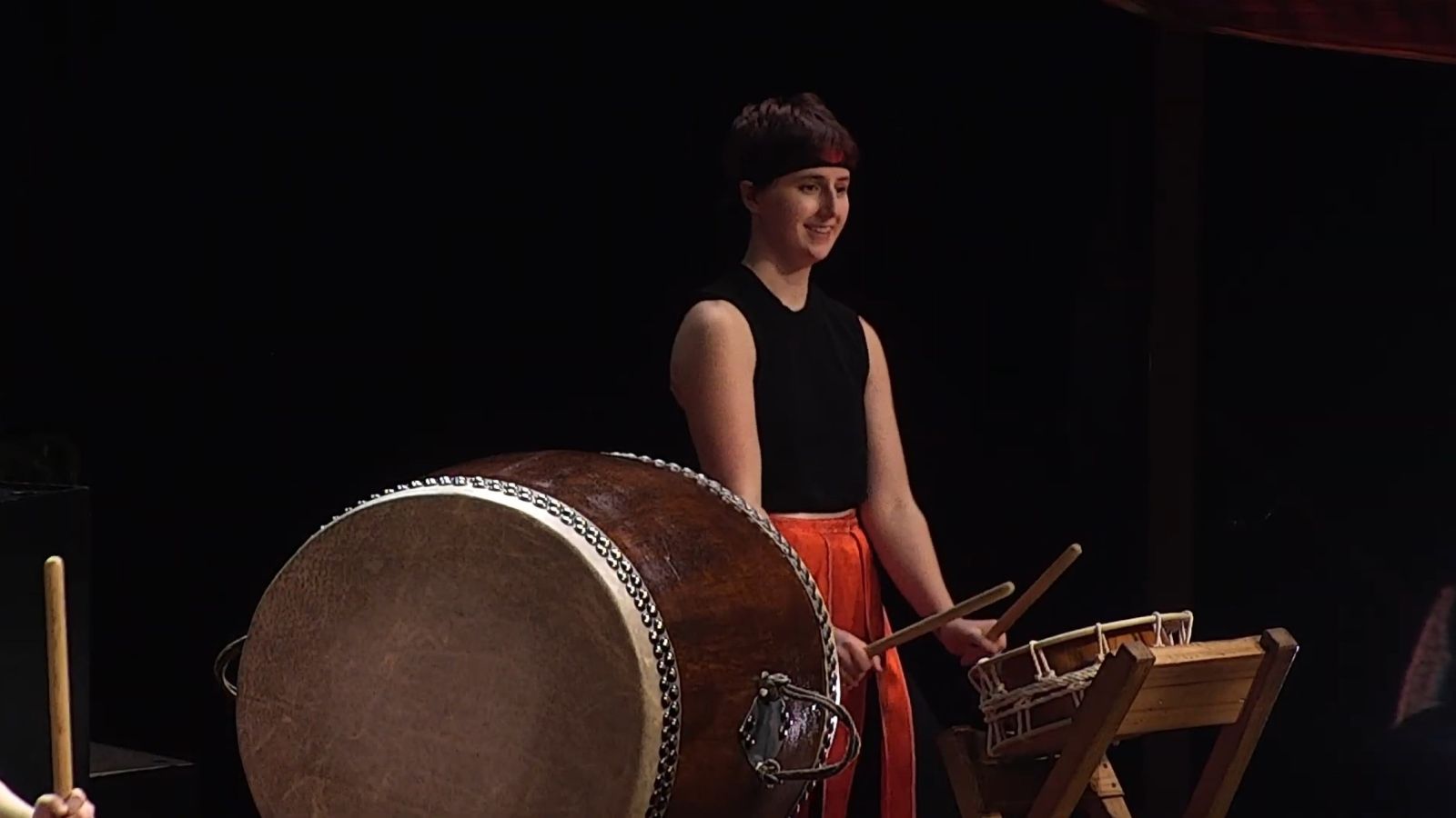 Person playing a large drum on stage during a ceremony.