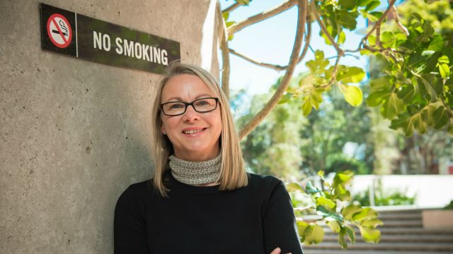 Uta Waterhouse stands in front of no smoking sign 