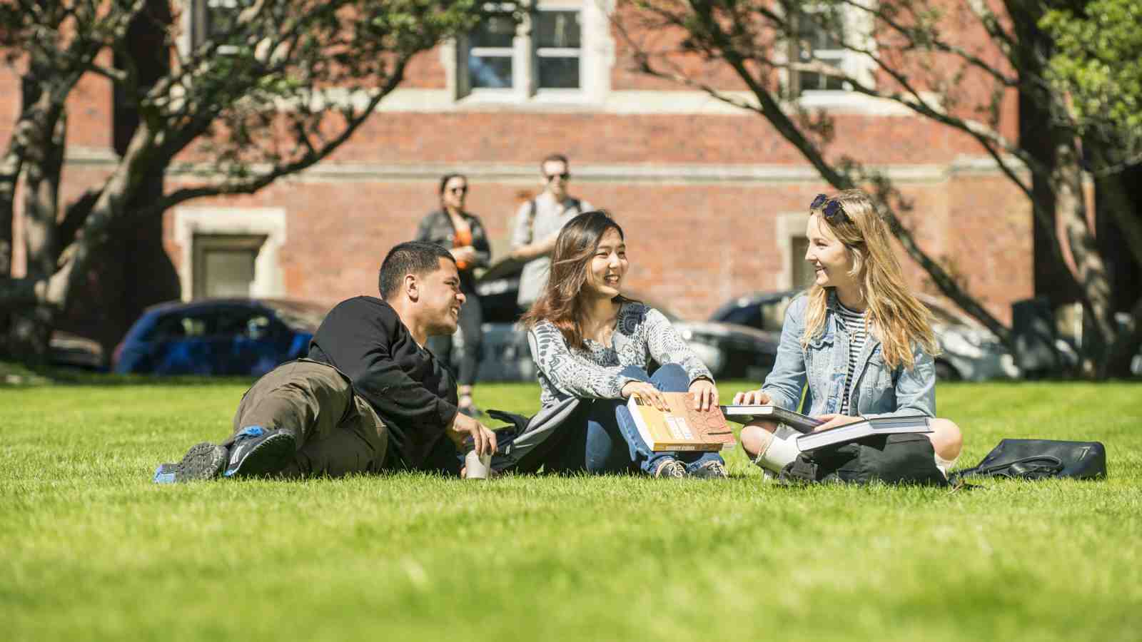 Three students sitting on the lawn in front of the Hunter Building at Victoria University’s Kelburn campus.