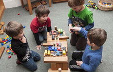 Four boys playing with blocks and toy cars.