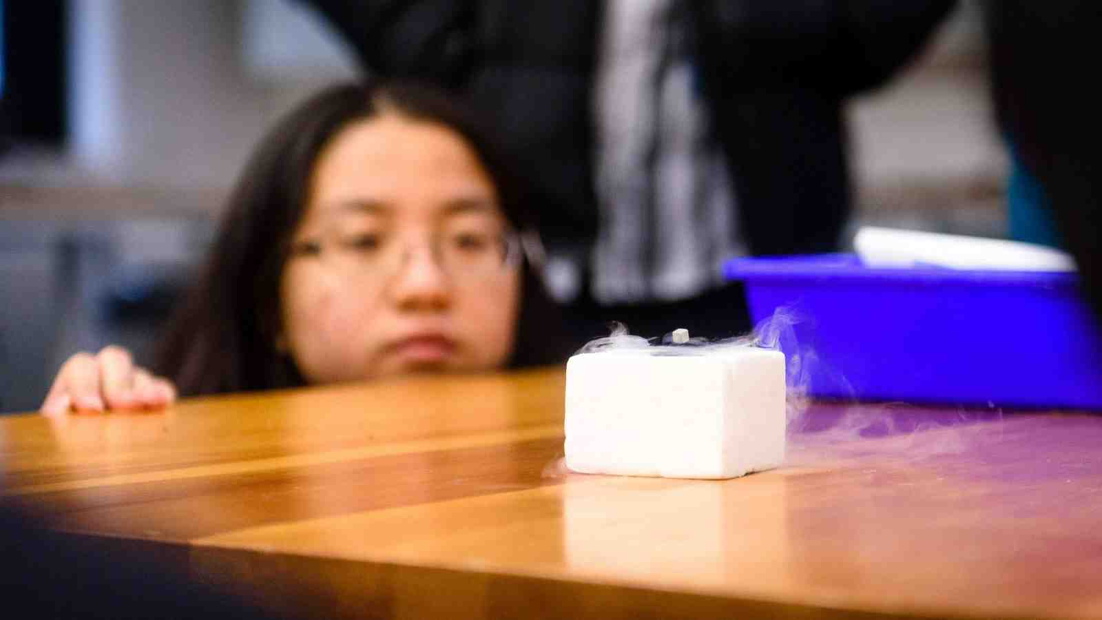 Young woman looks at magnetic cube levitating above a white box. 