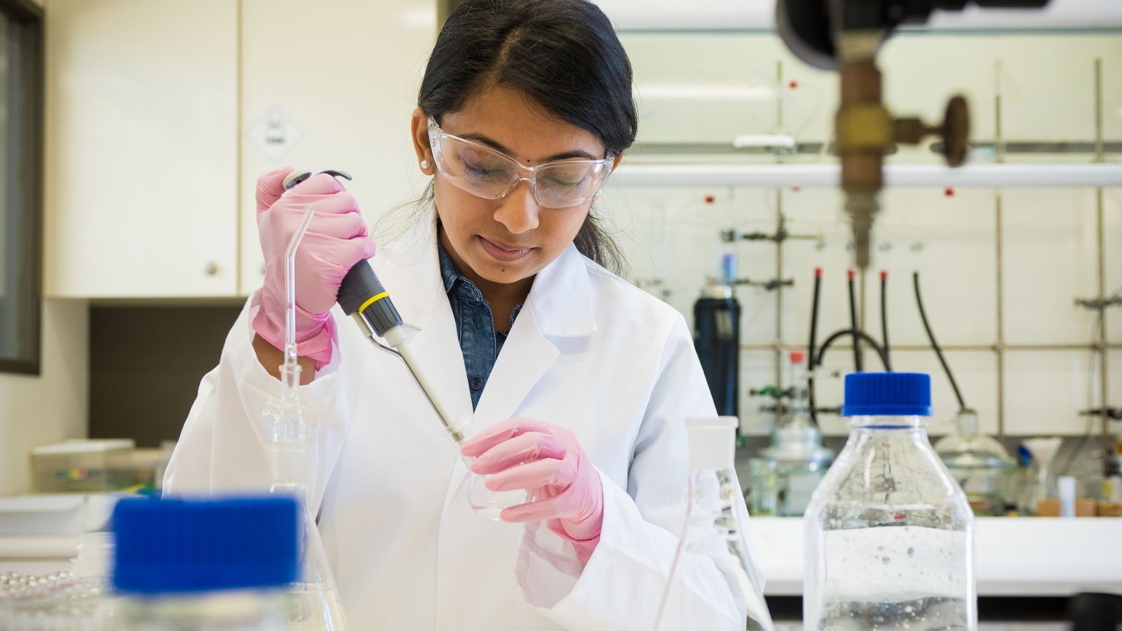 Research scientist adding liquid to glass flask.