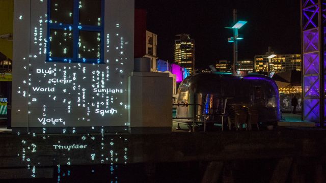 Words of light projected onto a building and Wellington harbour.