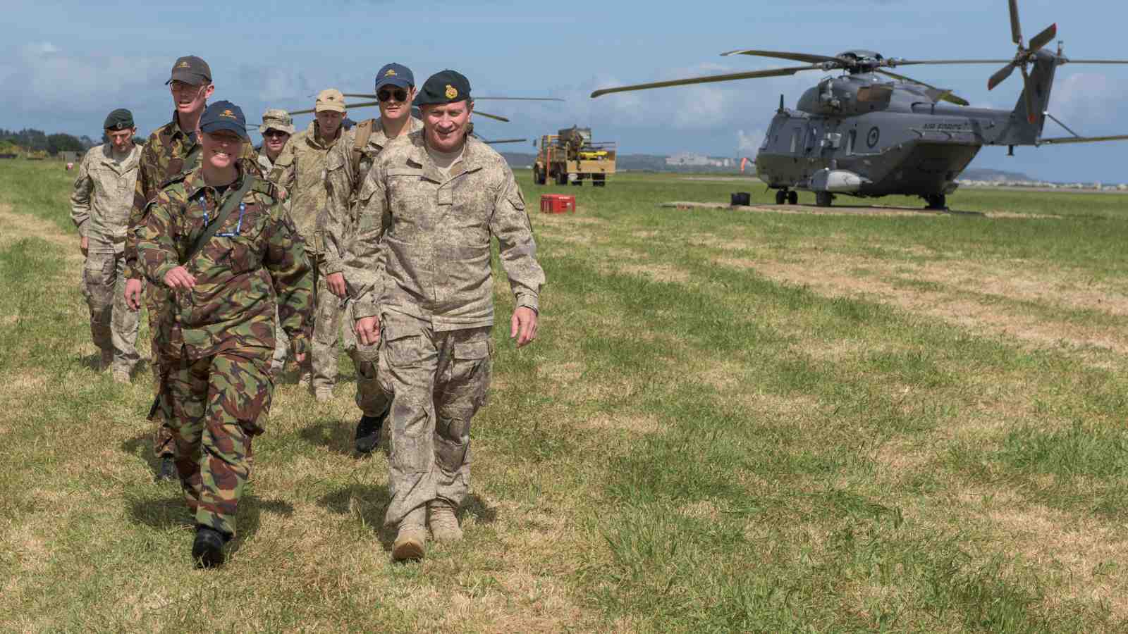 New Zealand soldiers walk by helicopters parked in an air field.