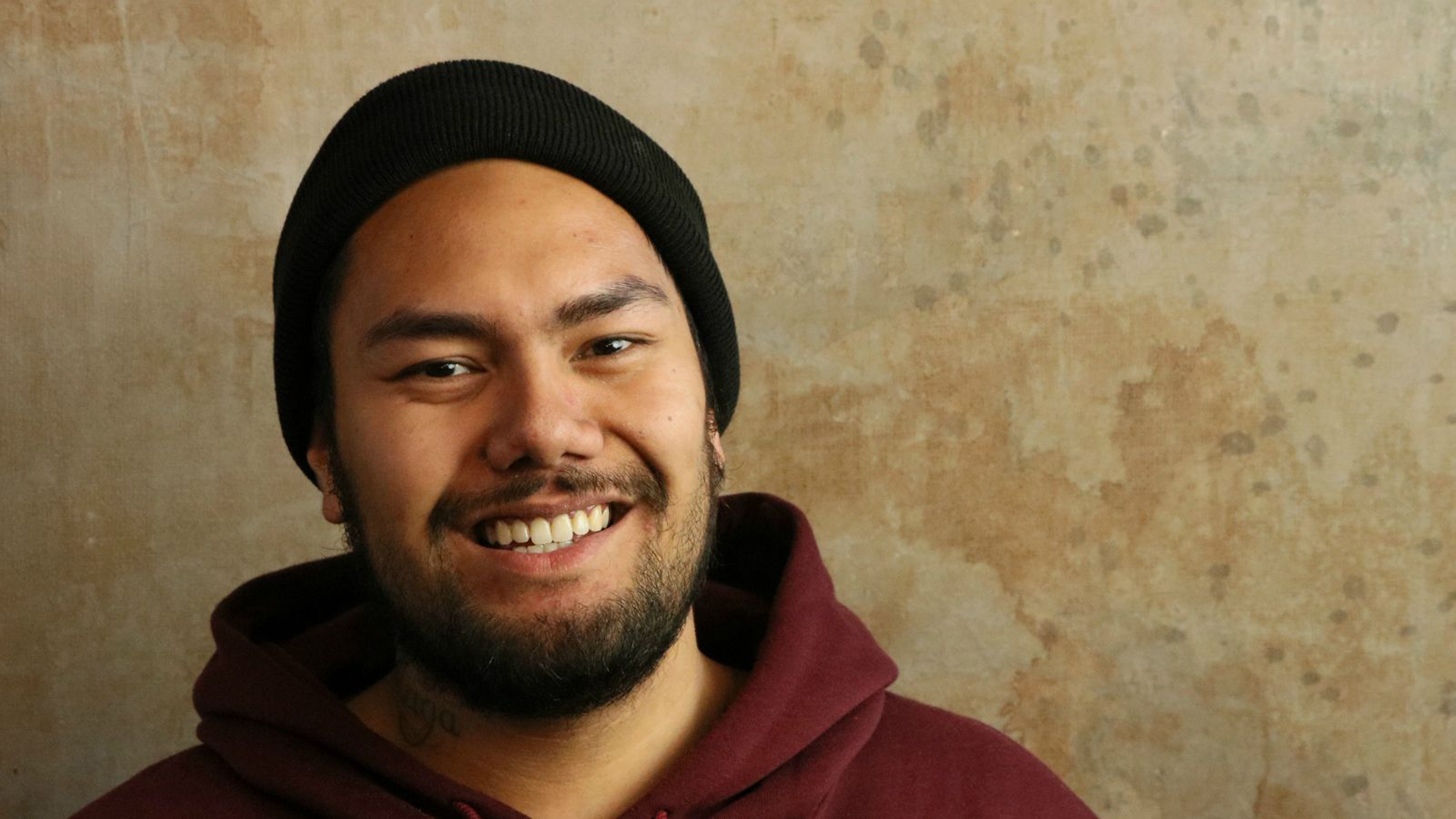 A smiling male student wears a royal red hoodie and a black beanie.