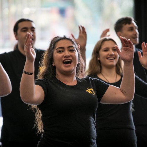 Two young men and two young women wearing black t-shirts singing with their arms raised.