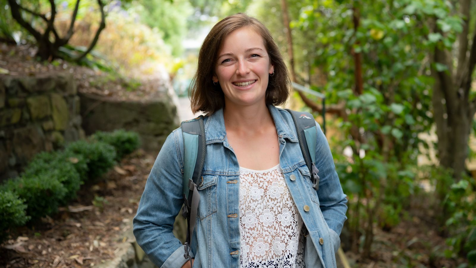 Ursula Featherstone stands smiling on a path in a wooded area.