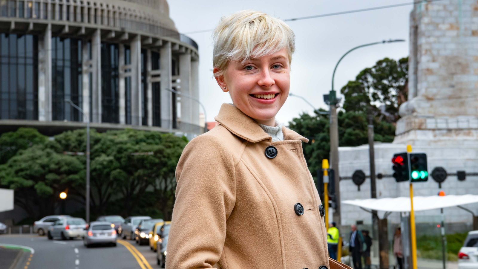 A student stands smiling in front of the Beehive in Wellington, New Zealand.