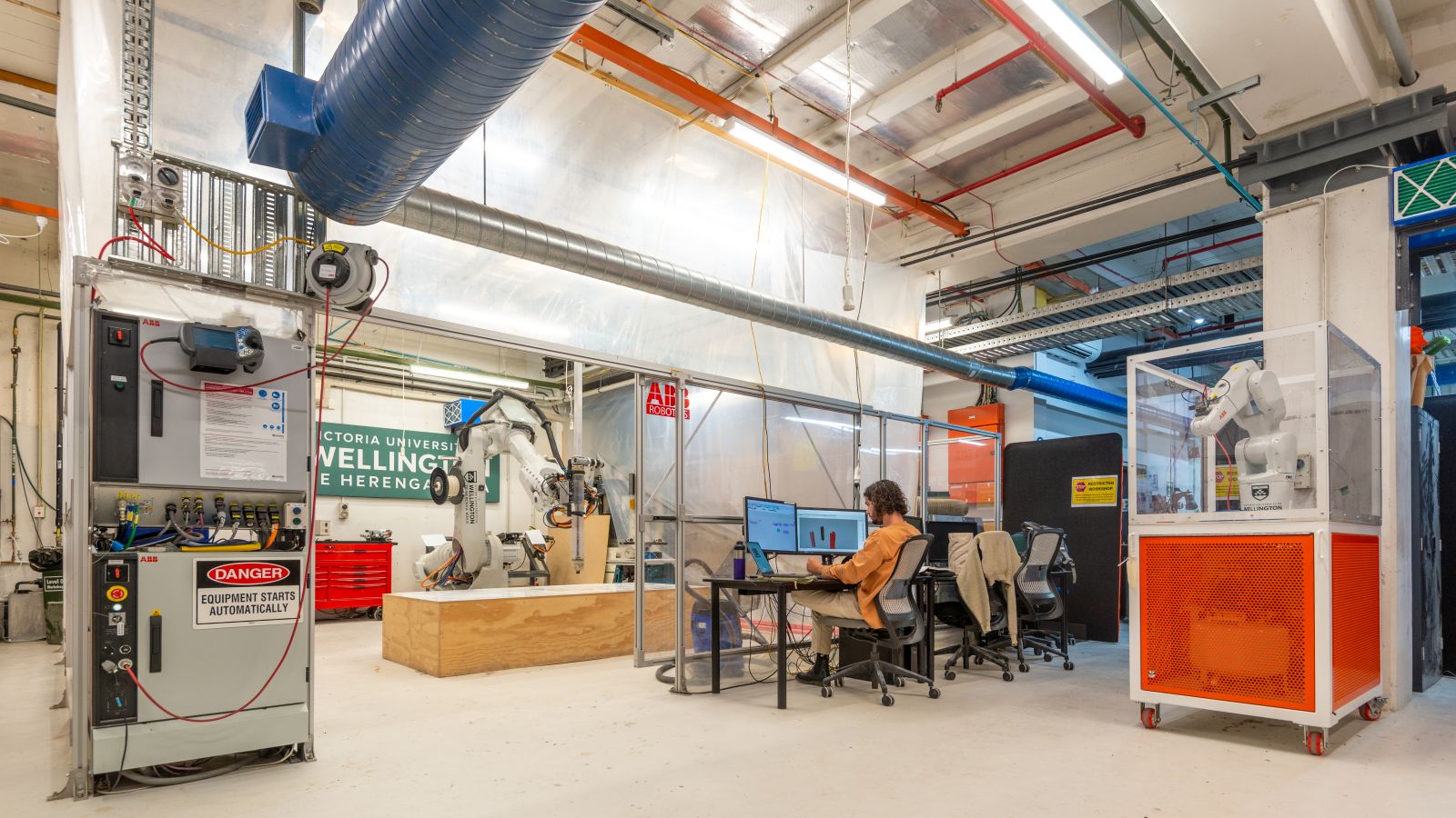 Student sat at computer in front of giant 3D printing robot arm in faculty 3D modelling workshop