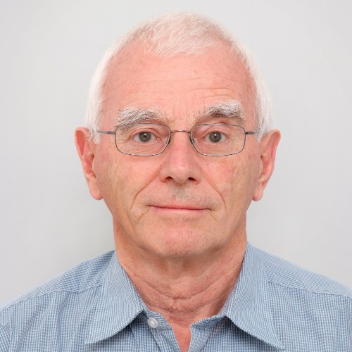 A man with glasses and white hair wearing a blue shirt, looking at the camera