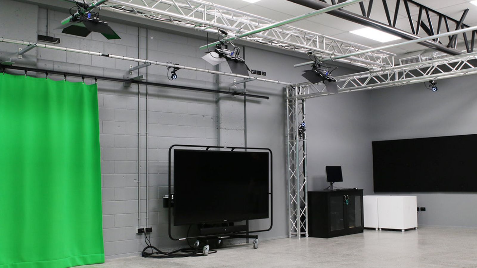 Studio with grey walls, green curtain, large screens.