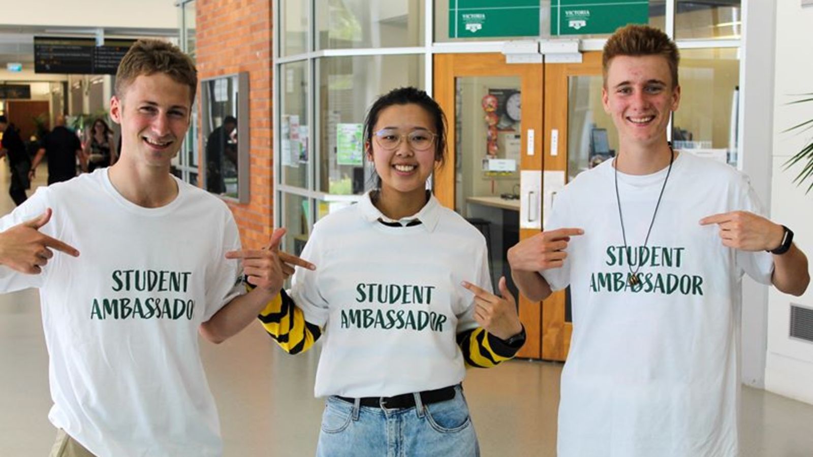 Student pointing at their t-shirts saying 'Student Ambassadors'.