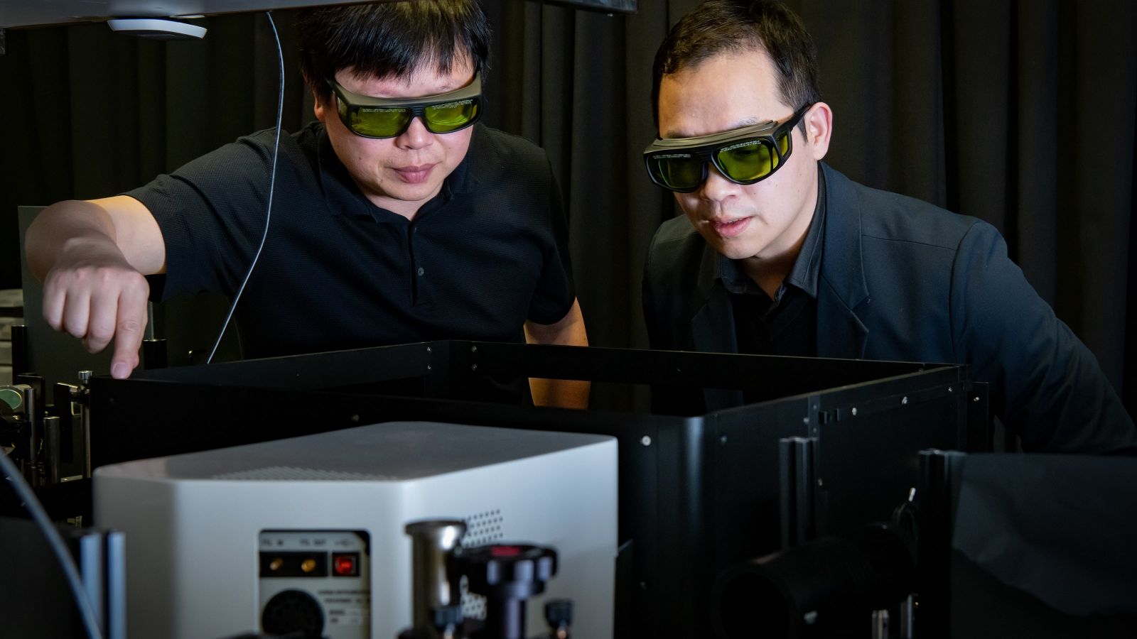 Two men wearing protective glasses looking at a laser spectroscopy machine in a dark room 