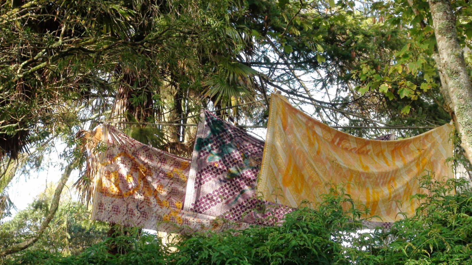 Three colourful pieces of cloth strung up in trees