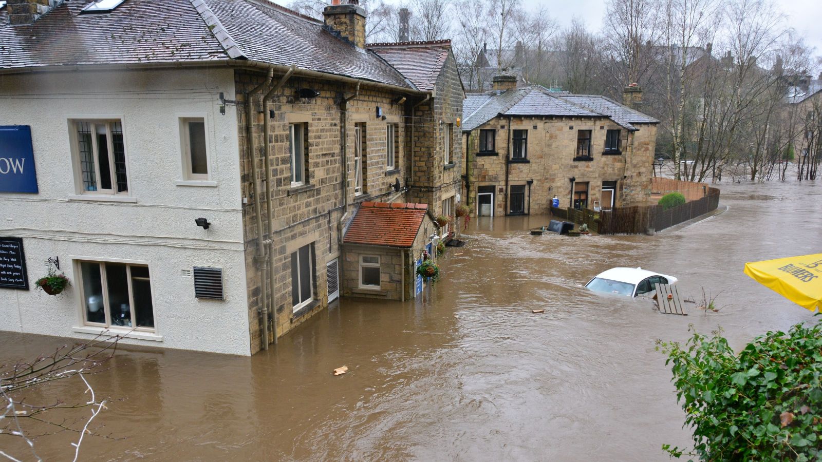 Brown flood water surrounds an old stone building with half-submerged cars