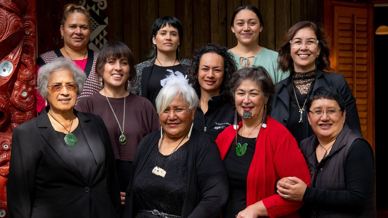 group of women out front of a marae with beautiful carvings 