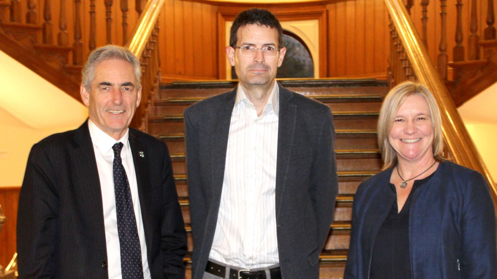 Simon Mackenzie inaugural lecture Vice-Chancellor Grant Guilford, new professor Simon Mackenzie, and dean of Humanities and Social Sciences Sarah Leggott, standing on a grand wooden staircase at Old Government Buildings.