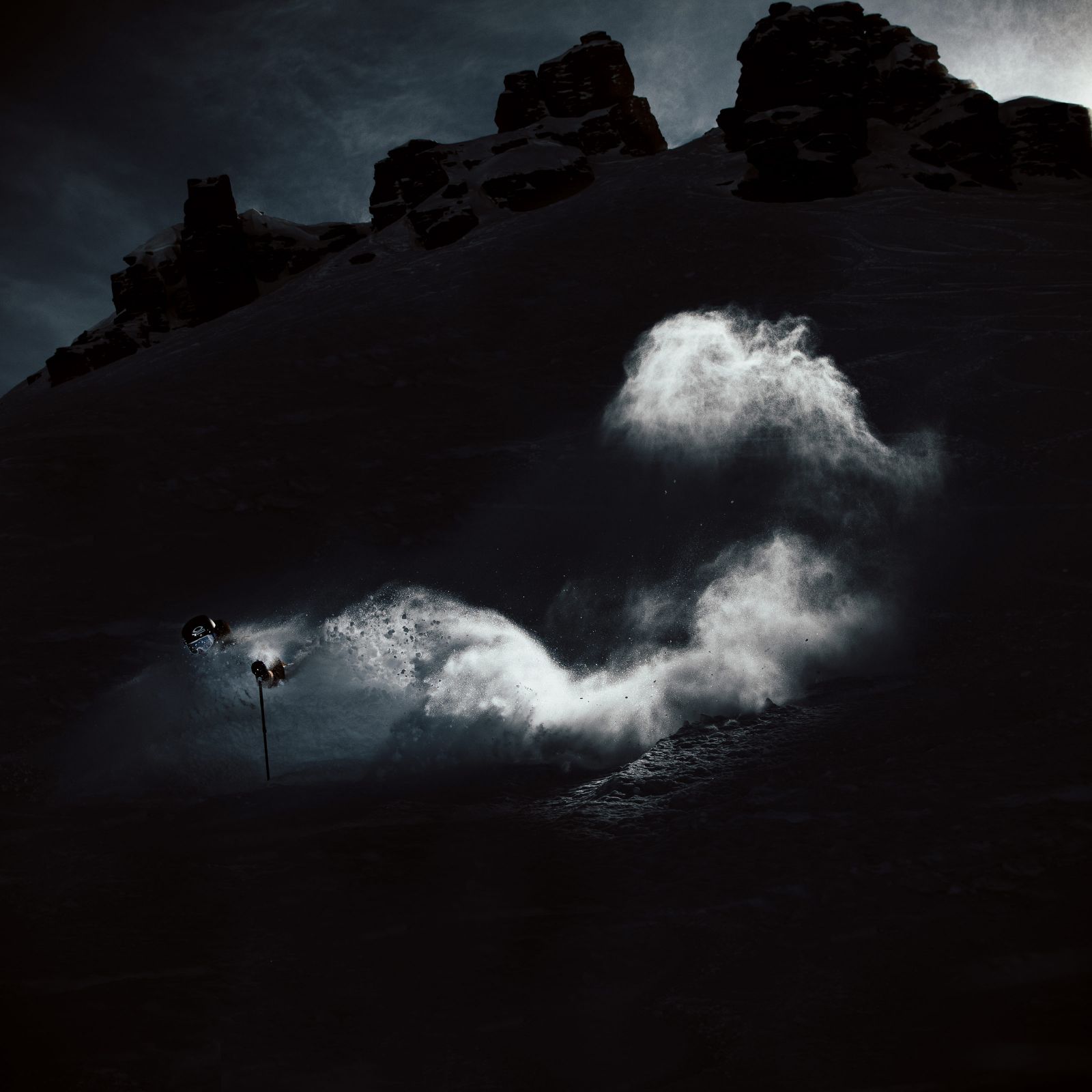 A cliff face with a skier going downhill with a cloud of snow following down the hill.