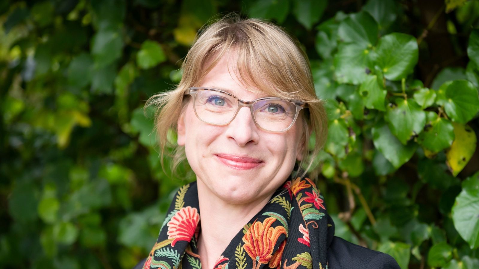 woman with blond hair tied back with colourful scarf and green background