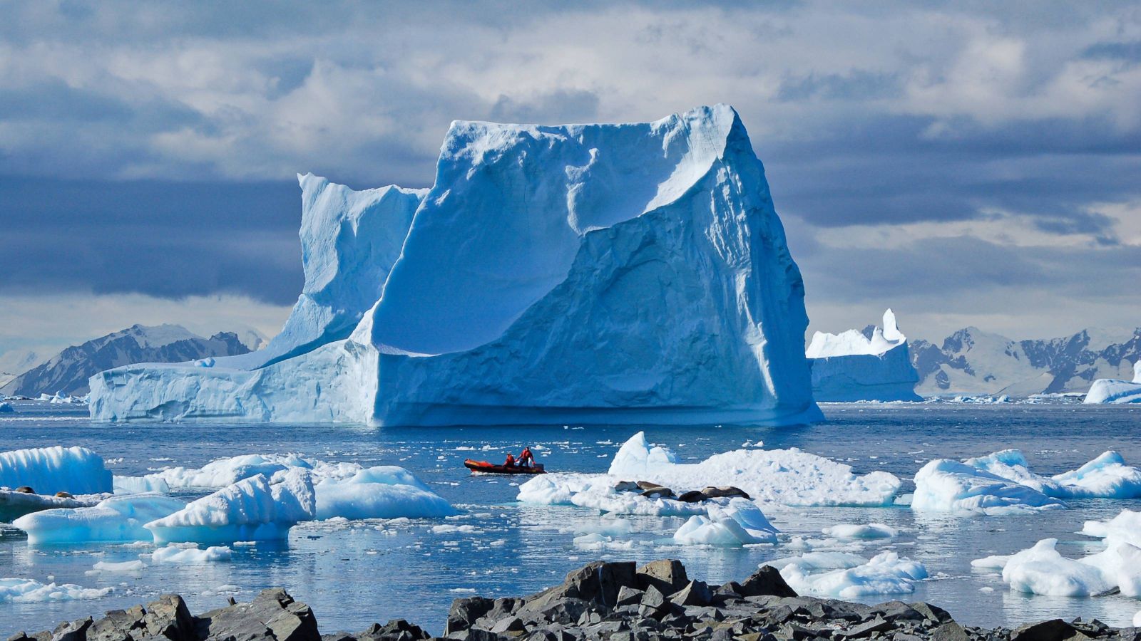 Small boat in water with large iceberg in the background. 