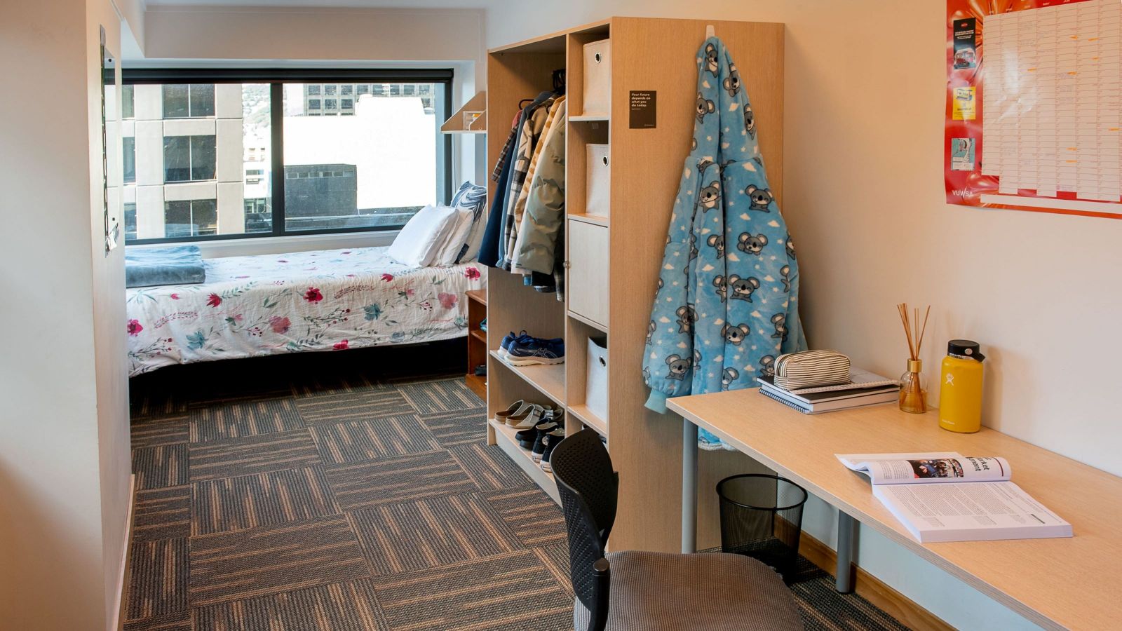 Single bedroom at Katharine Jermyn Hall with modern furnishings;a bed next to a large window, a wardrobe unit, desk and chair.