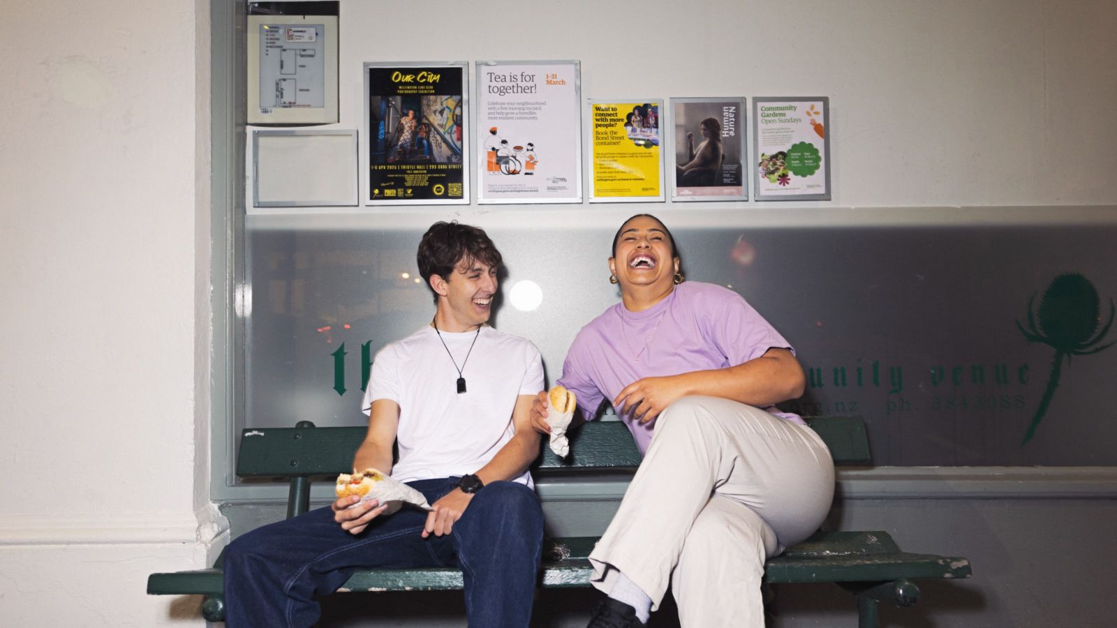 Two students sitting on a bench laughing, eating burgers 