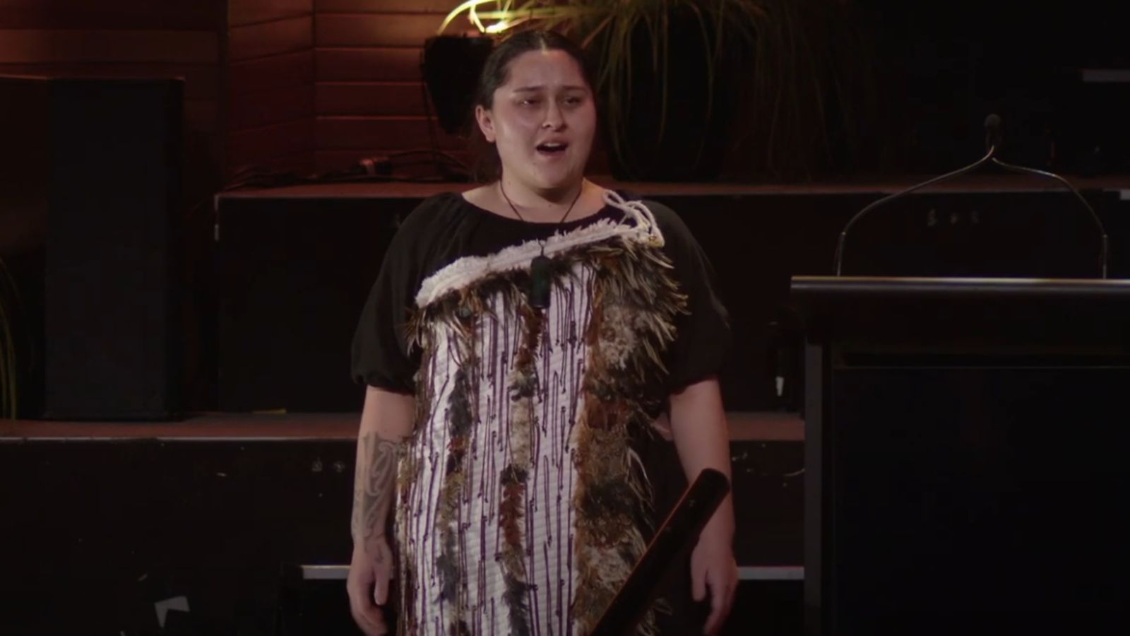 A woman in traditional Māori attire performs a ceremonial call (karanga) during a graduation ceremony.