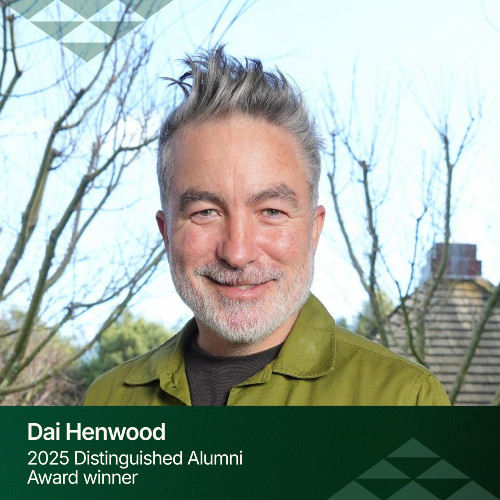 A close up of a smiling Dai Henwood with grey hair and a bright green shirt.