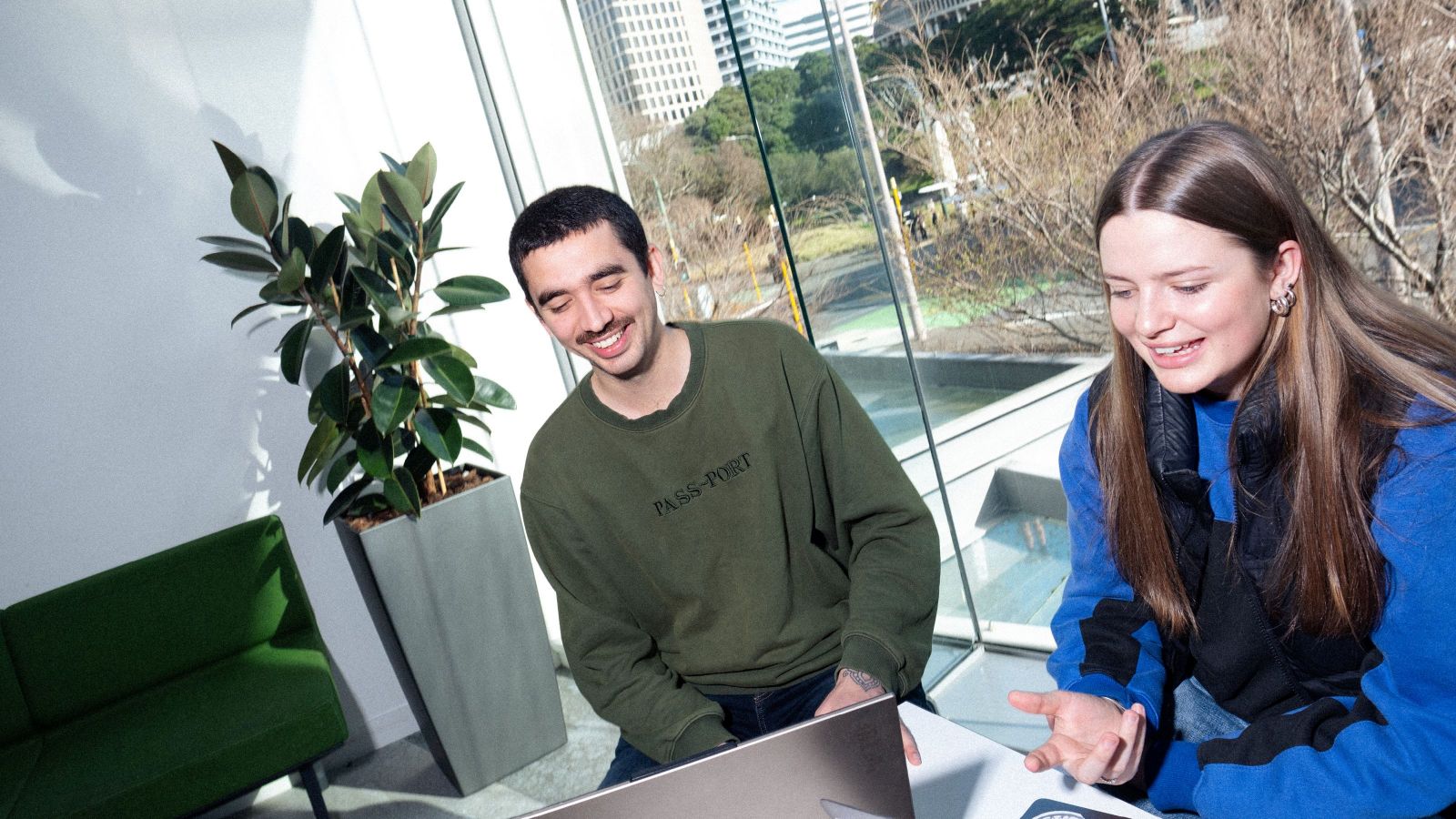 Students are sitting at a table in Rutherford House with the Beehive visible through the window