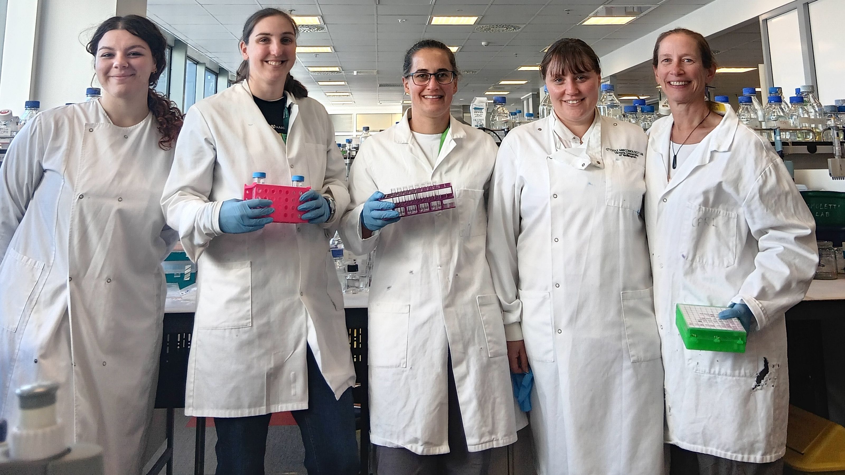 Women scientists standing in a row facing forward holding equipment.