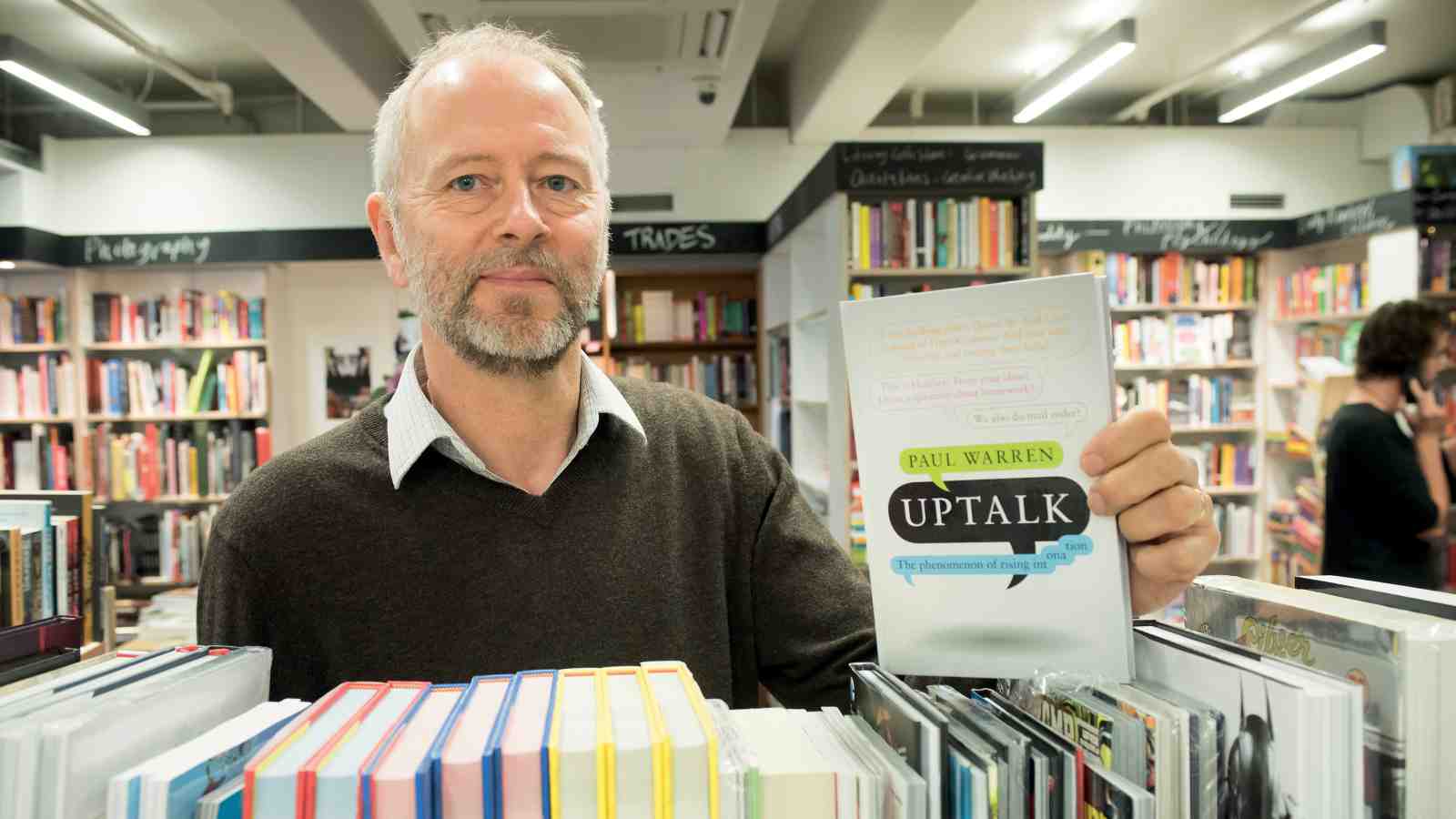 Associate Professor Paul Warren holding a copy of his book Uptalk in Kelburn campus Vic Books