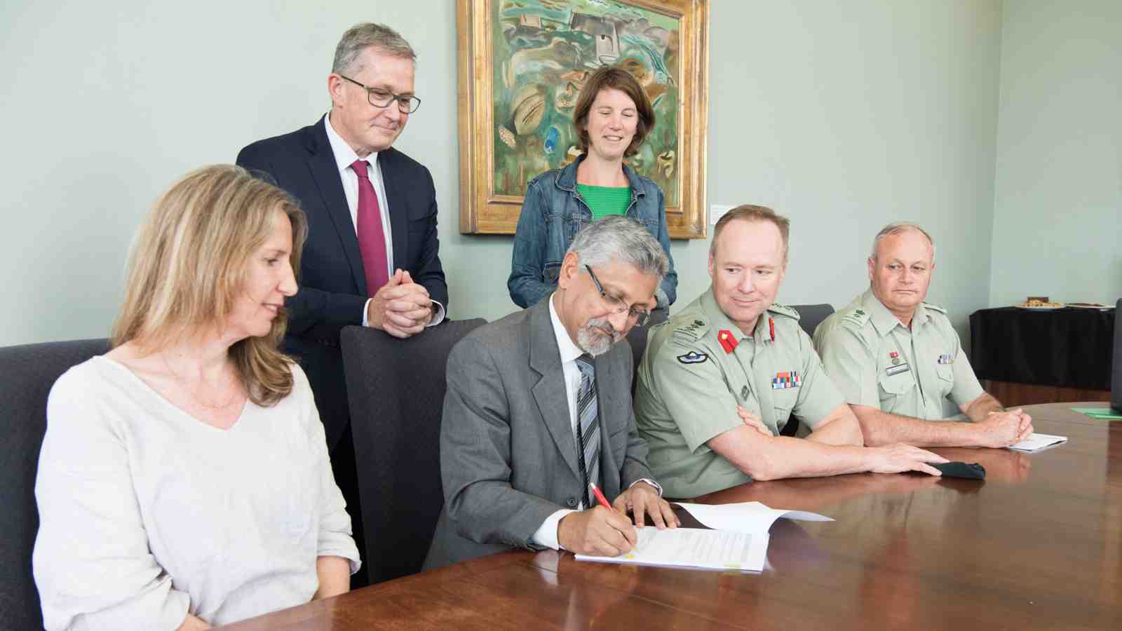 Victoria staff and Defence force staff at a table. A person in the middle is signing a document.