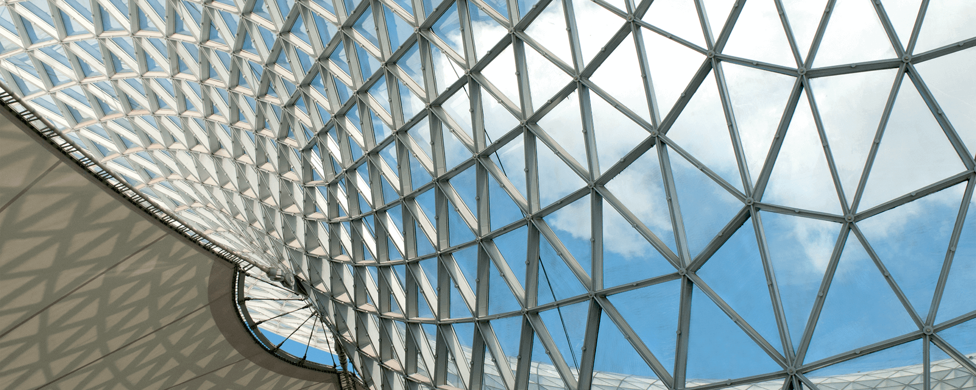 Image of a geometric roof made with glass and many triangles, showing a blus sky.