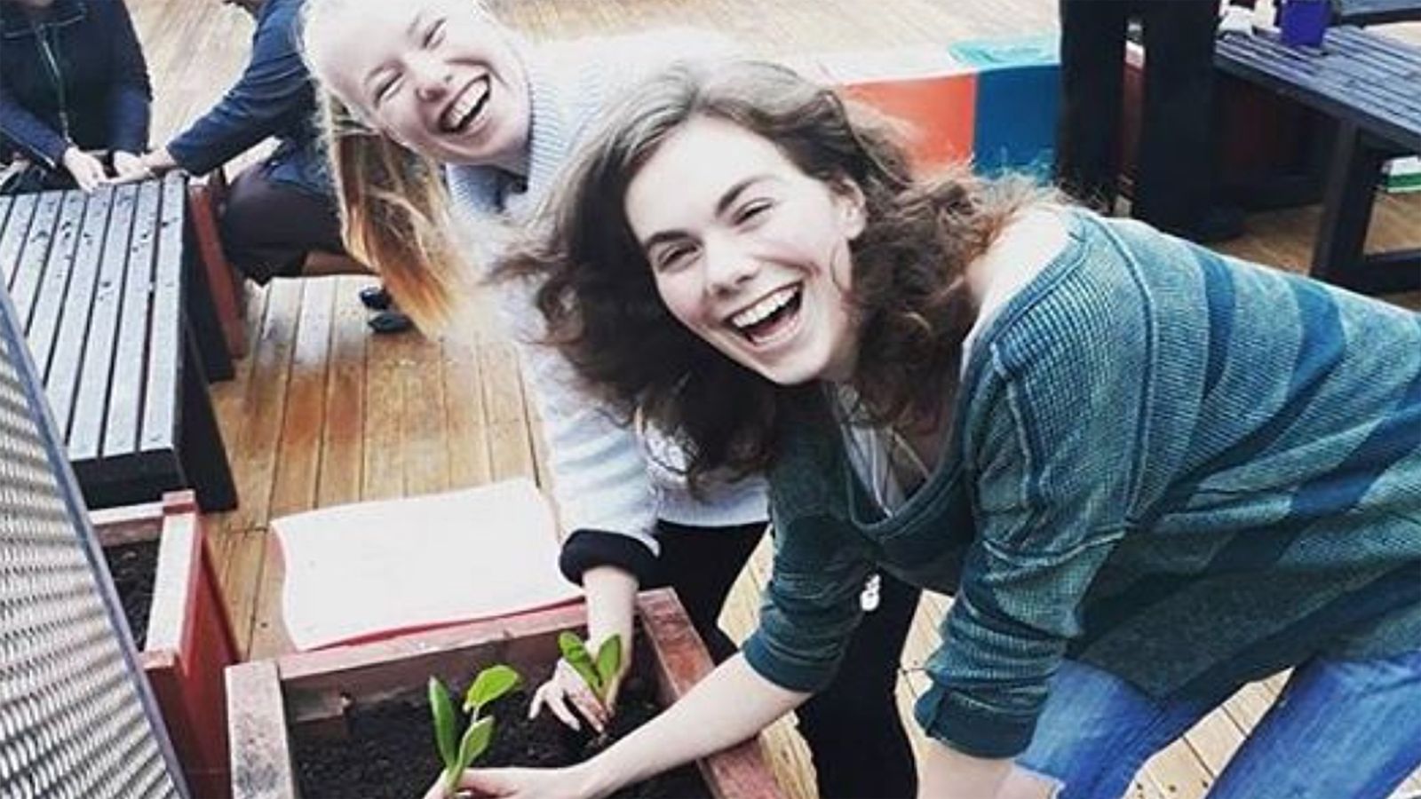 Two female students smile joyously while planting in raised bed.