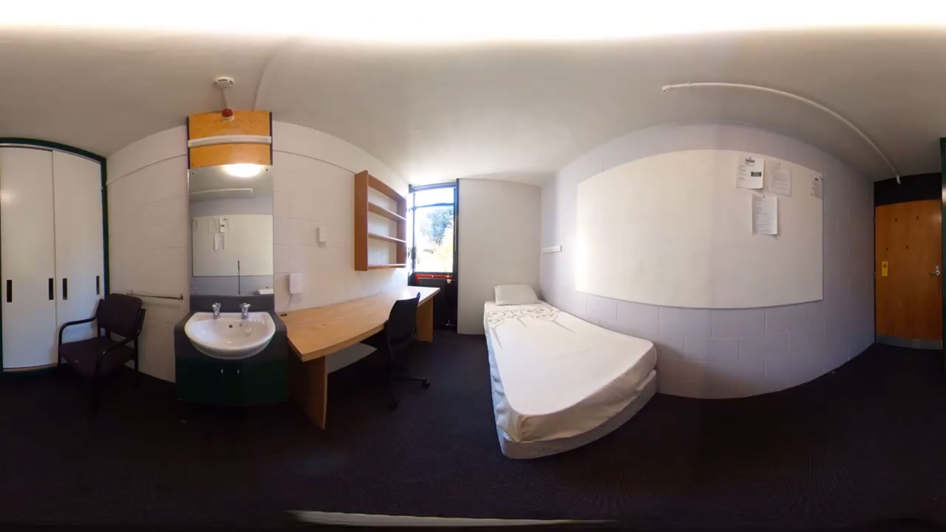 A panoramic view of a bedroom in the James Hutchinson wing with a single bed, a desk, and a sink.