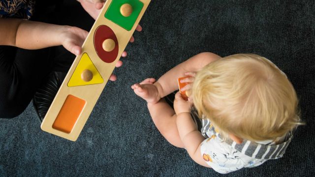 Birds-eye view of an instructor and child playing with a wooden puzzle.