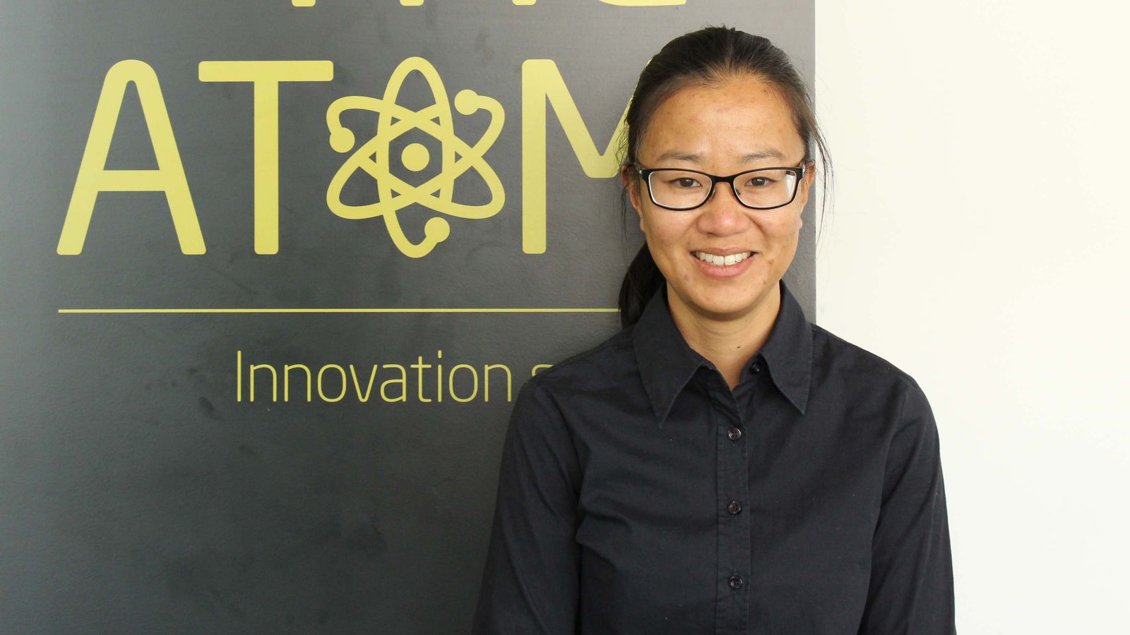 A profile image of Jessica Lai standing by a banner the reads, The Atom.