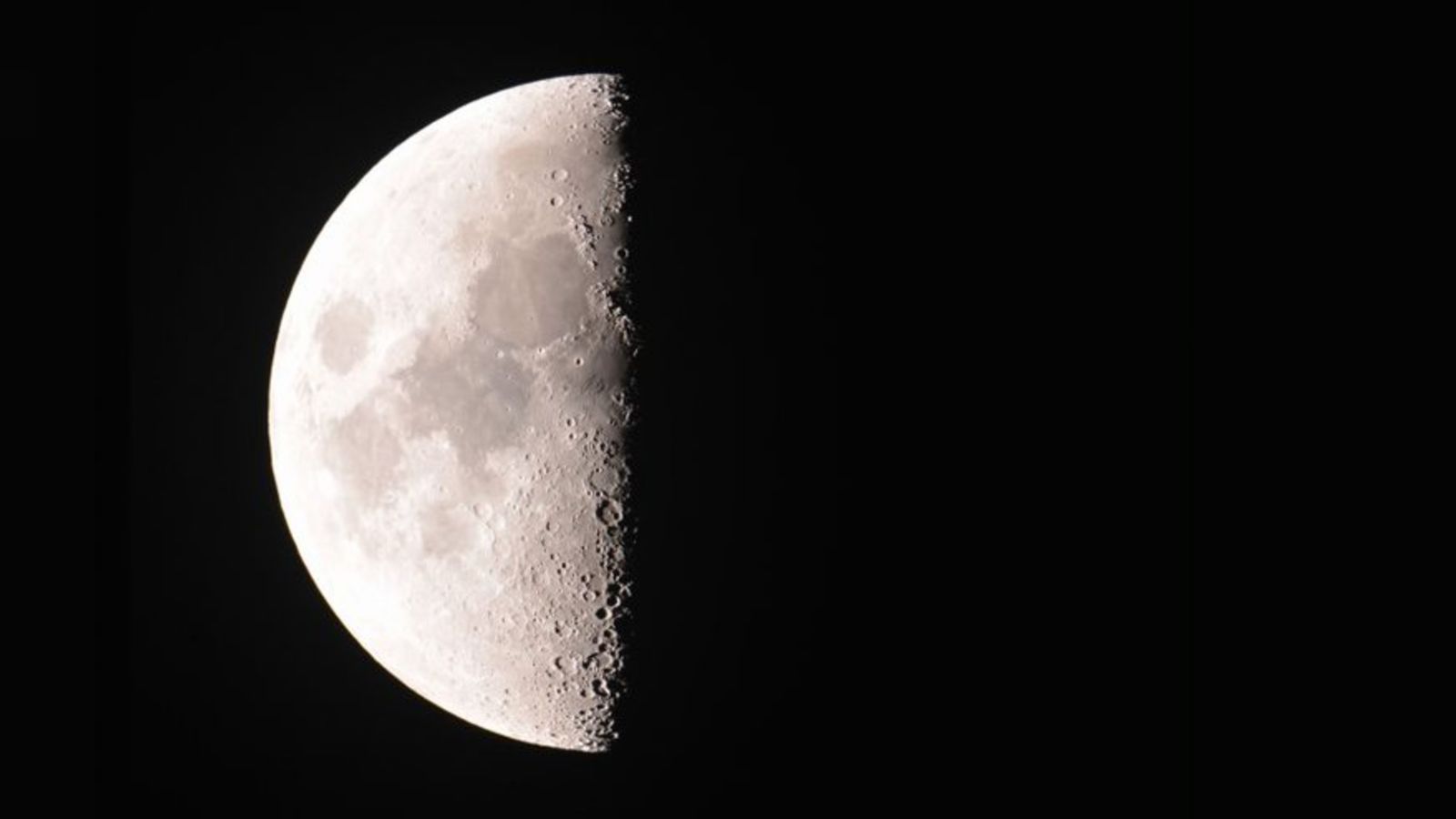 Real image of a half moon, the left side of the moon is illuminated and the rest of the image is pitch black.