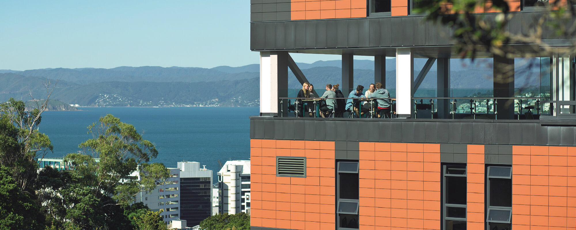 A group of students sitting in the dining room of Te Puni Village hall of residence which overlooks Wellington harbour.