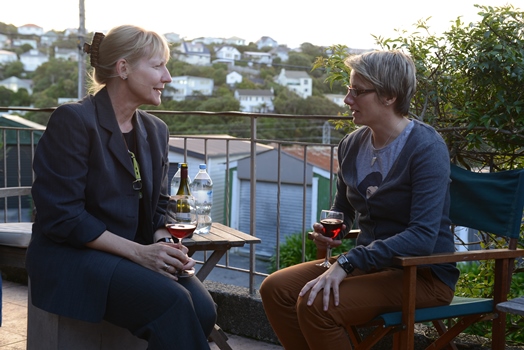 Two professional women convers on a balcony with a view of a lush green residential area in the background.