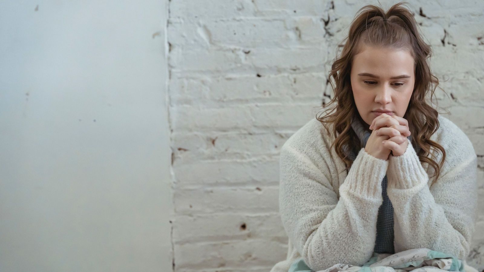 girl with curly hair and cream jersey sitting against white wall