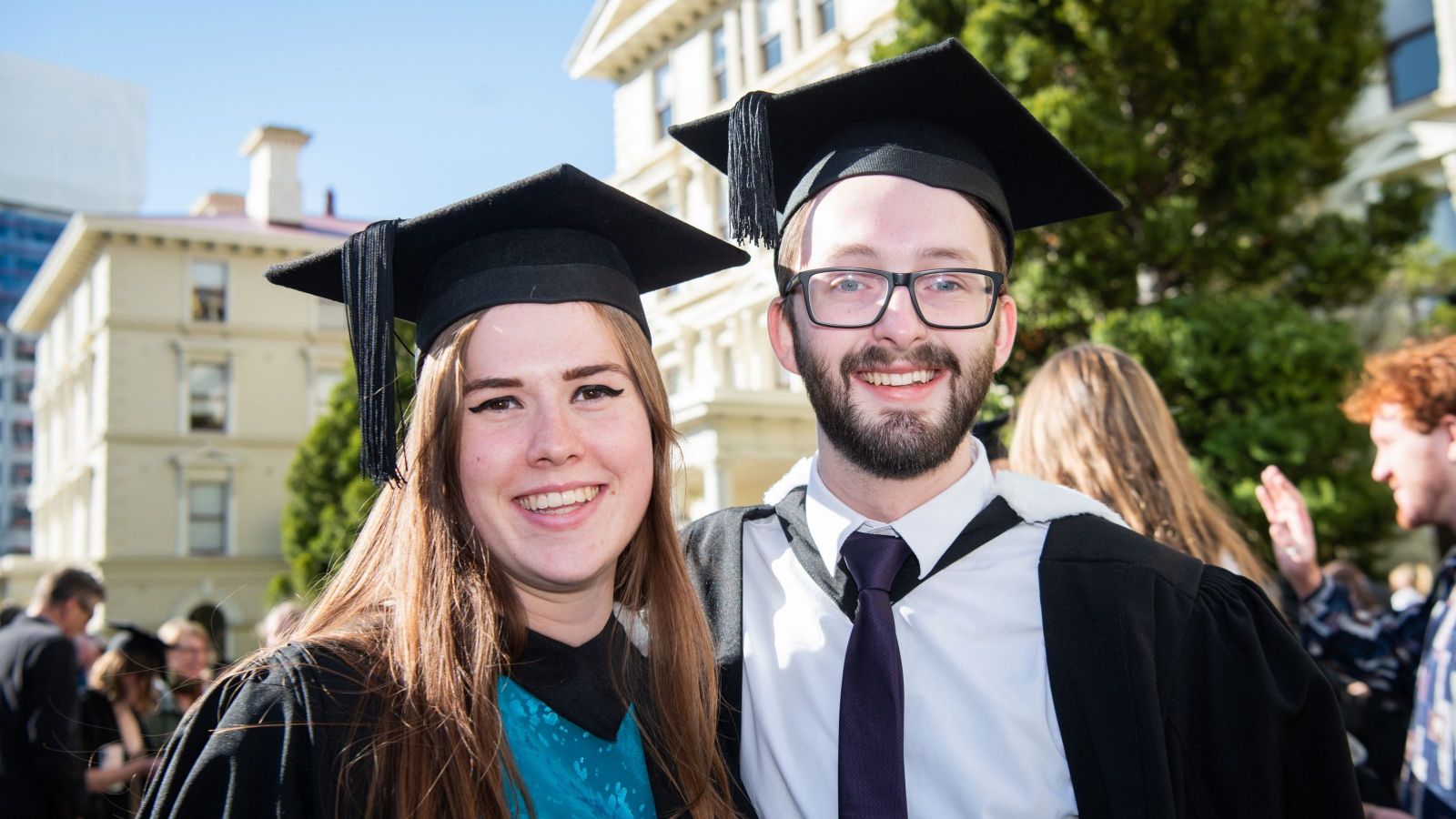 woman and man wearing trencher hats with smiles and graduation gowns