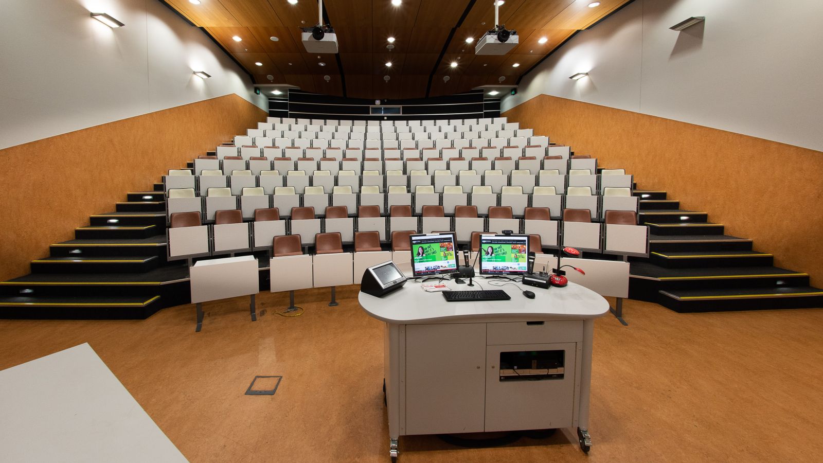 Small lecture theatre from the front, with computer screens on front lectern visible