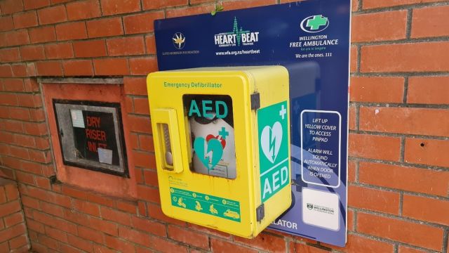 Yellow emergency defibrillator box mounted on brick wall.