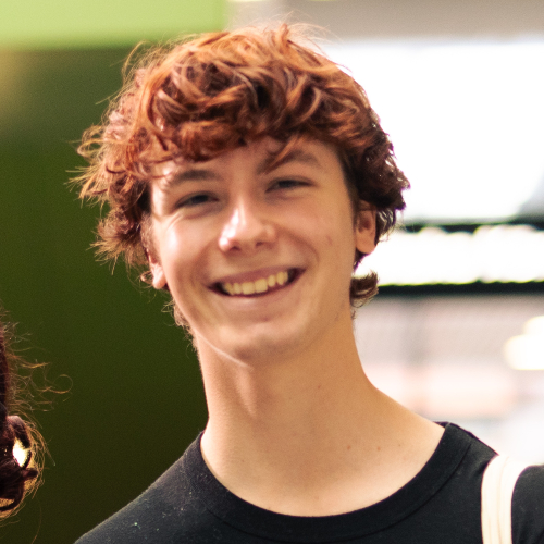 A head and shoulders portrait of a smiling, male student with red hair