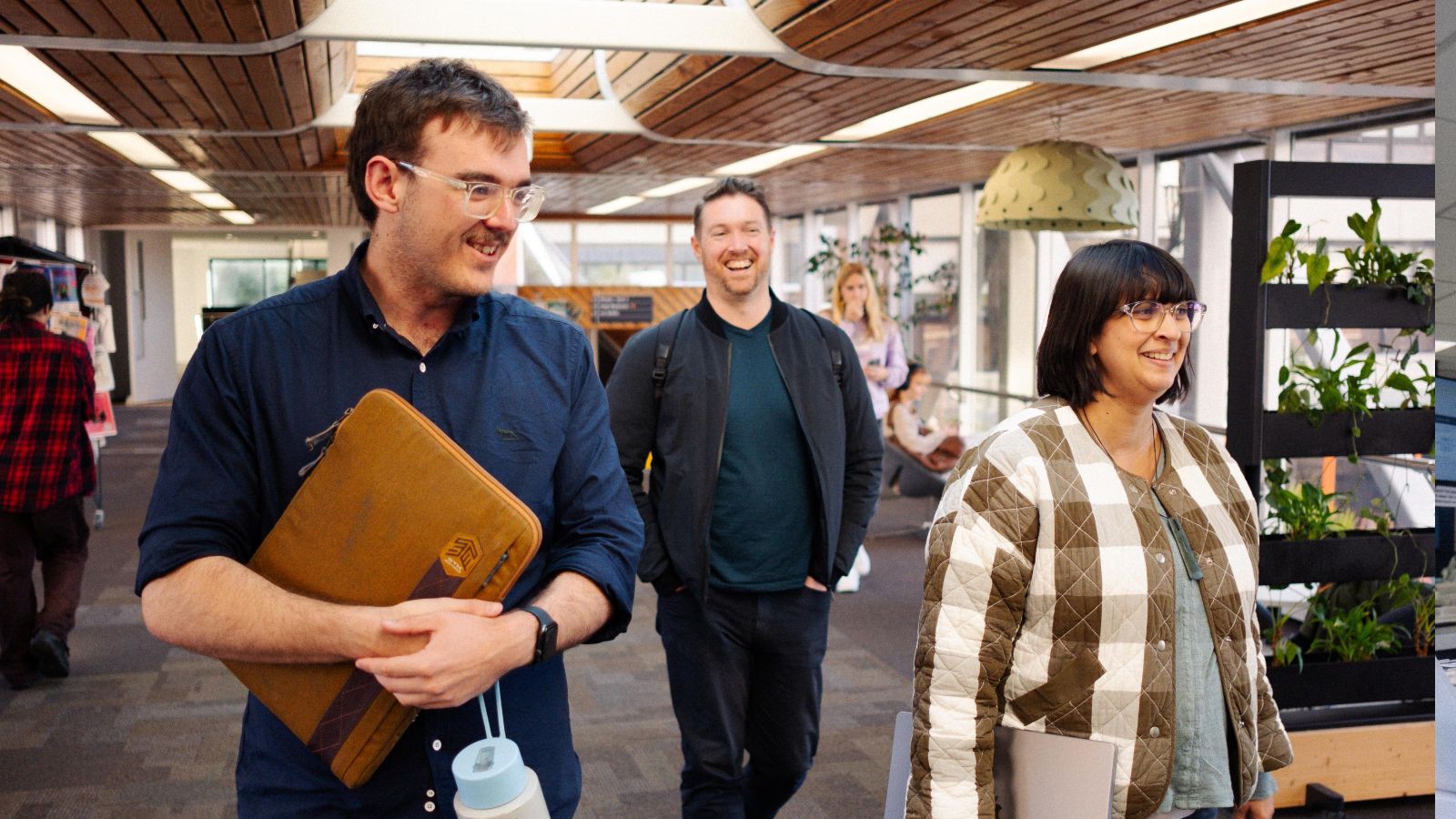 3 people walking through a bright campus building carrying laptops