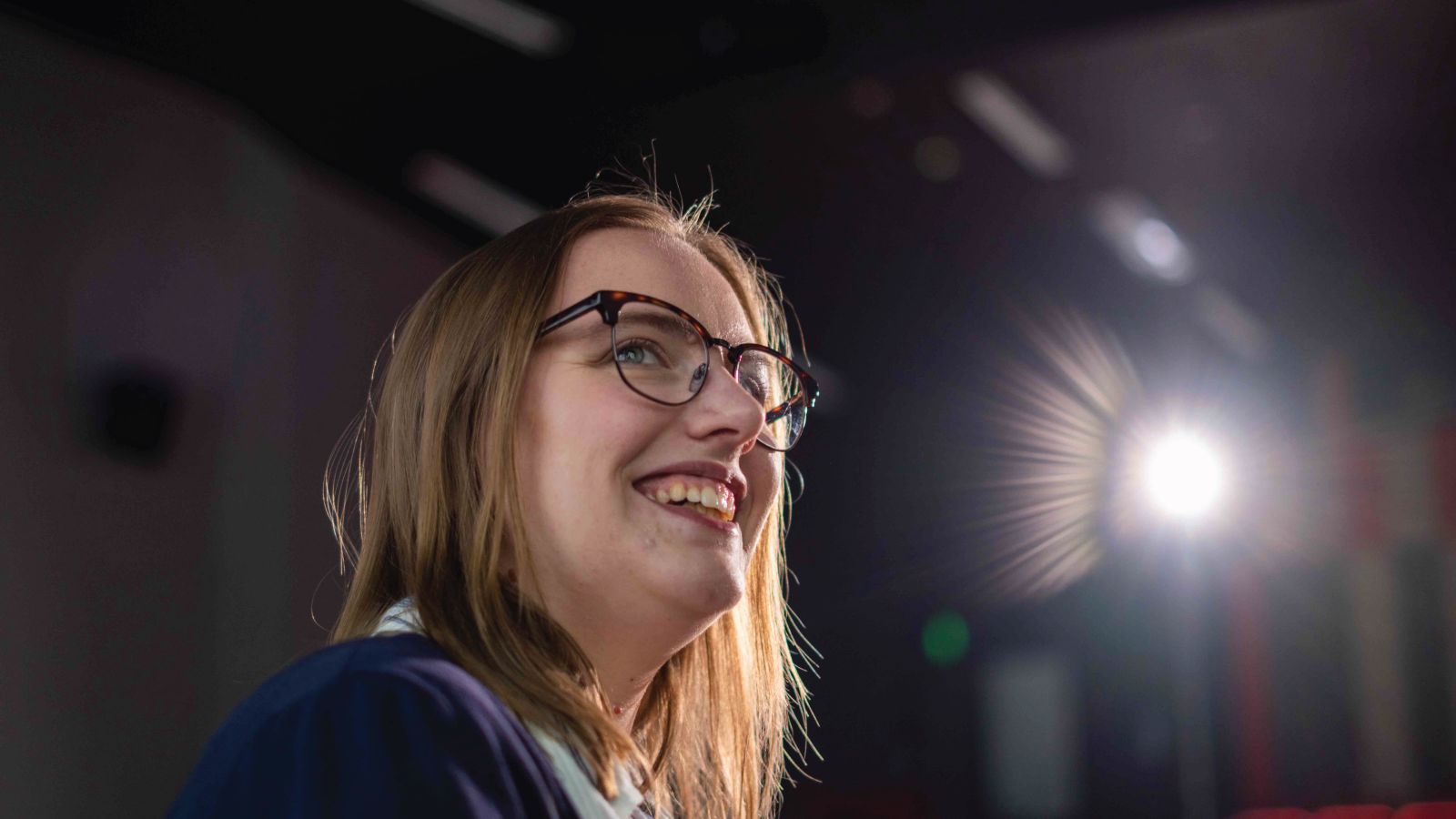 Student in a lecture theatre with a projector spotlight streaming into the camera.