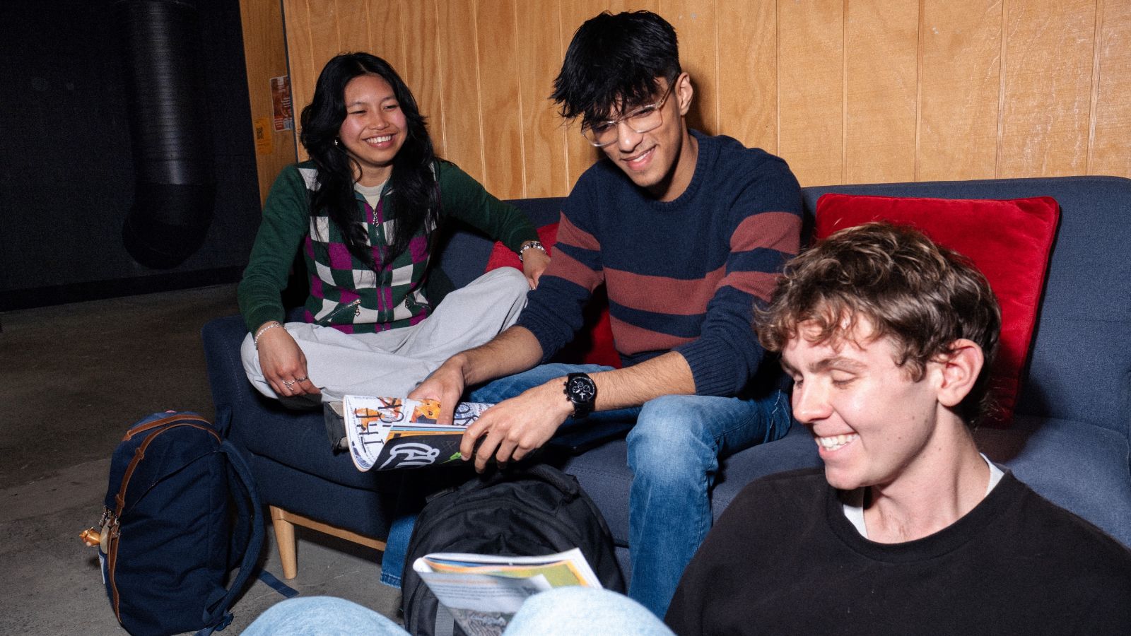 Three students sitting on a couch in uni building reading magazines
