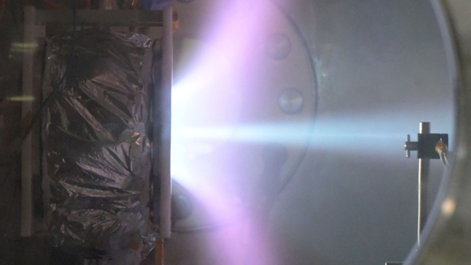 Purple-blue plasma plume inside a laboratory vacuum chamber.