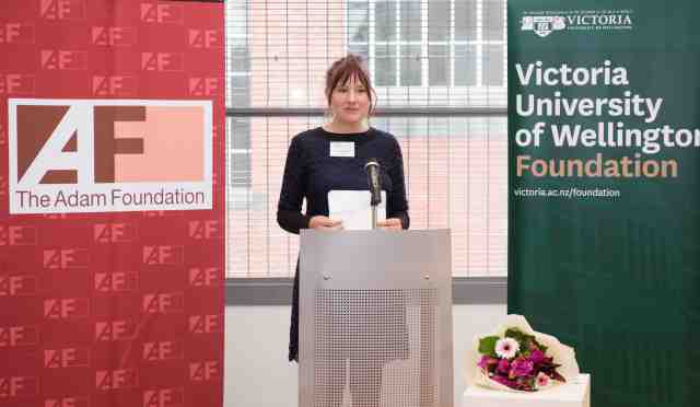 Annaleese stands behind a podium giving an speech.